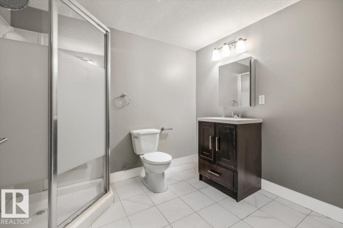 Shower enclosure with frosted glass, dark wood-finish vanity with white countertop, chrome hardware, and white tile flooring - 1090 Armitage Crescent Sw, Edmonton, AB 