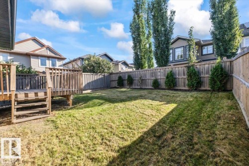 Rear yard featuring a wooden deck with railing, natural grass, and a wooden privacy fence - 1090 Armitage Crescent Sw, Edmonton, AB 