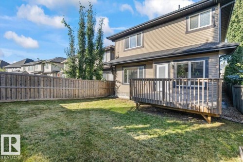 Expansive backyard with a wooden fence, mature trees, and a raised wood-plank deck with railing - 1090 Armitage Crescent Sw, Edmonton, AB 
