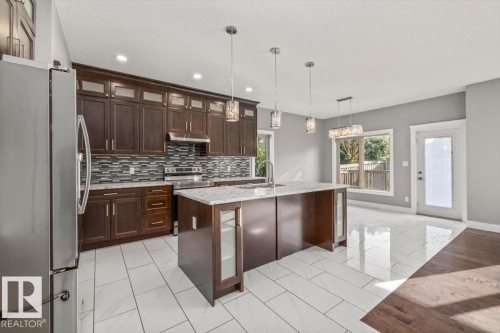 Kitchen featuring dark wood cabinetry, stainless steel appliances, a tile backsplash, a kitchen island with a stone countertop, and pendant lighting - 1090 Armitage Crescent Sw, Edmonton, AB 