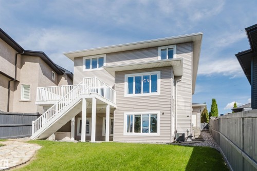 Multi-level residence featuring a rear deck with white railings and stairs, a manicured lawn, and extensive window placements - 3412 Macneil Link Nw, Edmonton, AB 