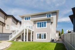 Multi-level residence featuring a rear deck with white railings and stairs, a manicured lawn, and extensive window placements - 