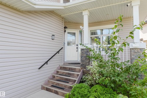 Siding exterior with a covered porch featuring stone-clad pillars, white railing, and a tile-step entry - 3412 Macneil Link Nw, Edmonton, AB 