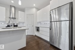 Modern kitchen with white cabinetry, stainless steel appliances, wood-finish flooring, and a subway tile backsplash - 