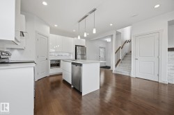Open-concept kitchen with a central island, stainless steel appliances, wood-finish flooring, and white cabinetry - 