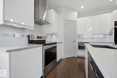 Sleek white cabinetry, stainless steel appliances, light-toned countertops, and wood-finish flooring - 8952 81 Avenue Nw, Edmonton, AB 
