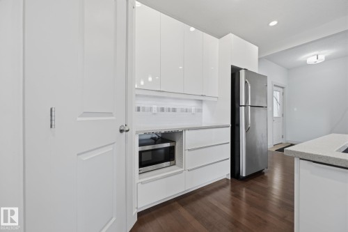 White panel door, white cabinetry, dark wood-finish flooring, stainless steel refrigerator, and built-in microwave - 8952 81 Avenue Nw, Edmonton, AB 
