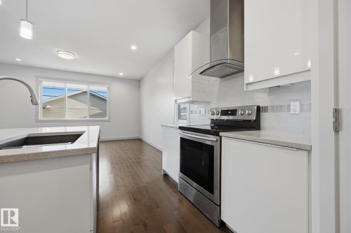 Modern kitchen featuring a stainless steel range and hood, white flat-panel cabinetry, light-toned countertop, and wood-finish flooring - 8952 81 Avenue Nw, Edmonton, AB 