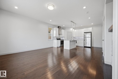 Open-concept living area featuring rich wood-finish flooring, recessed lighting, and a modern kitchen - 8952 81 Avenue Nw, Edmonton, AB 