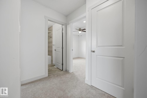 Carpeted hallway with white interior doors, a contemporary ceiling fan, and a bathroom featuring tiled walls and flooring - 8952 81 Avenue Nw, Edmonton, AB 