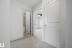 Carpeted hallway with white interior doors, a contemporary ceiling fan, and a bathroom featuring tiled walls and flooring - 