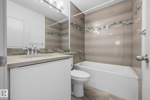 Bathroom featuring a vanity with an integrated sink, a large wall mirror, a tiled shower/tub combination with a decorative accent band, and wood-finish floor tiling - 8952 81 Avenue Nw, Edmonton, AB 