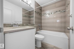 Bathroom featuring a vanity with an integrated sink, a large wall mirror, a tiled shower/tub combination with a decorative accent band, and wood-finish floor tiling - 