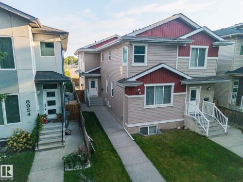 Two-story residence featuring light-toned siding with red accent panels, multiple windows, and a concrete pathway - 8952 81 Avenue Nw, Edmonton, AB 