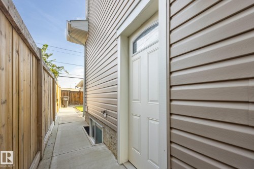 Tan horizontal siding with white trim, a privacy fence, a concrete walkway, and a white exterior door with an arched window - 8952 81 Avenue Nw, Edmonton, AB 