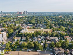 Expansive urban landscape with extensive tree canopy, diverse residential architecture, multistory apartment buildings, and distant city skyline - 