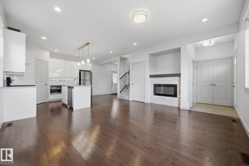 Open-concept living area featuring wood-finish flooring, a contemporary kitchen with a central island, a built-in fireplace with a stone surround, and an integrated appliance suite - 8952 81 Avenue Nw, Edmonton, AB 