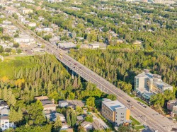 Aerial perspective showcasing extensive tree coverage, multi-lane roadway, diverse residential structures, and commercial properties - 