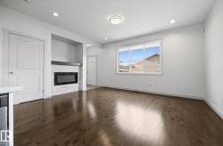 Wood-finish flooring, a contemporary electric fireplace with a stacked stone surround, a dark wood mantel, recessed lighting, and a large window - 