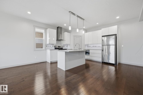 Open-concept kitchen with a central island, stainless steel appliances, white cabinetry, and wood-finish flooring - 8952 81 Avenue Nw, Edmonton, AB 