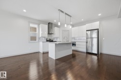 Open-concept kitchen with a central island, stainless steel appliances, white cabinetry, and wood-finish flooring - 