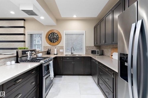 Modern kitchen with dark cabinetry, light countertops, and stainless steel appliances - 9654 100 Street Nw, Edmonton, AB 