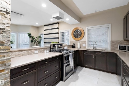 Stainless steel gas range, dark wood-finish cabinetry, light-toned countertops, tile backsplash, and recessed lighting - 9654 100 Street Nw, Edmonton, AB 