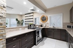 Stainless steel gas range, dark wood-finish cabinetry, light-toned countertops, tile backsplash, and recessed lighting - 