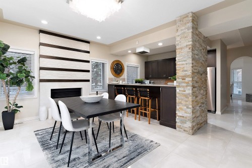 Modern fireplace with a decorative mantel, light-toned large format floor tiles, recessed lighting, and a stone-clad architectural feature - 9654 100 Street Nw, Edmonton, AB 