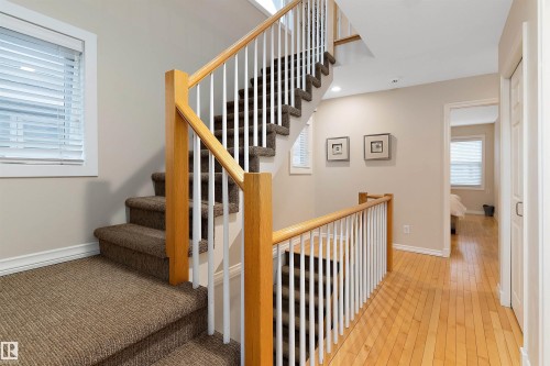 Carpeted staircase with wood handrails, white spindles, and light-tone wood flooring on the upper landing - 9654 100 Street Nw, Edmonton, AB 