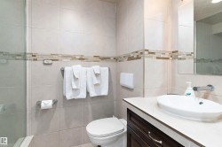 Tiled bathroom with a glass shower enclosure, decorative tile accent band, vanity with an integrated basin sink, and a wall-mounted faucet - 
