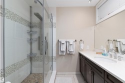 Glass-enclosed shower with a rainfall showerhead, mosaic tile accents, and a stone-tiled floor - 