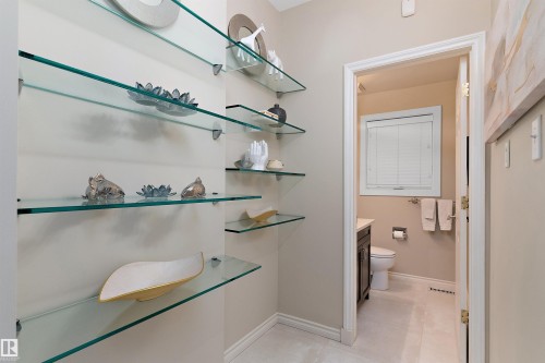 Built-in glass shelving, neutral wall paint, and a white trim doorway leading to a half-bath with a window - 9654 100 Street Nw, Edmonton, AB 
