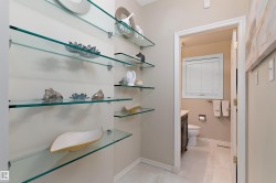 Built-in glass shelving, neutral wall paint, and a white trim doorway leading to a half-bath with a window - 