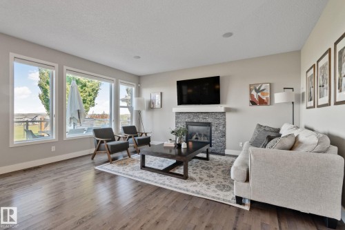 Wood-finish flooring throughout, a stone-clad fireplace with a white mantel, numerous windows, and recessed lighting - 2096 Redtail Common Nw, Edmonton, AB 