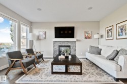 Spacious living area featuring a stone-clad fireplace with a mantel, large windows, recessed ceiling lighting, and wood-finish flooring - 