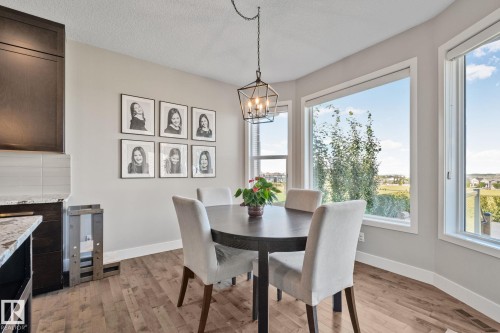 Bright dining area showcasing a round black table, upholstered dining chairs, and a pendant light fixture suspended from the ceiling - 2096 Redtail Common Nw, Edmonton, AB 
