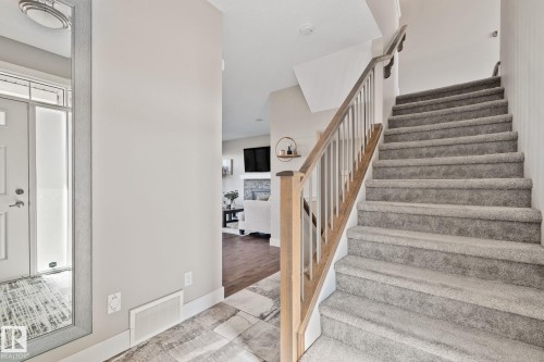 Carpeted staircase with wood handrail, tiled foyer flooring, and a front entry door with transom and sidelight windows - 2096 Redtail Common Nw, Edmonton, AB 