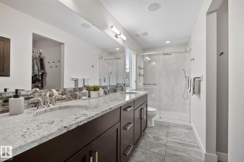Dual vanity with stone countertop, dark wood-finish cabinetry, tile flooring, and a glass-enclosed shower with a tiled surround - 2096 Redtail Common Nw, Edmonton, AB 