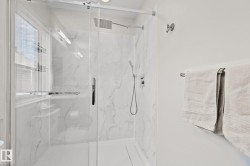 Walk-in shower with clear glass enclosure, marble-finish wall panels, and chrome fixtures including a rain showerhead and handheld sprayer - 