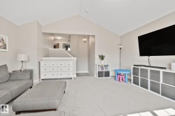 Vaulted ceiling, neutral wall paint, carpeted flooring, upper-level hallway, and a contemporary light fixture - 