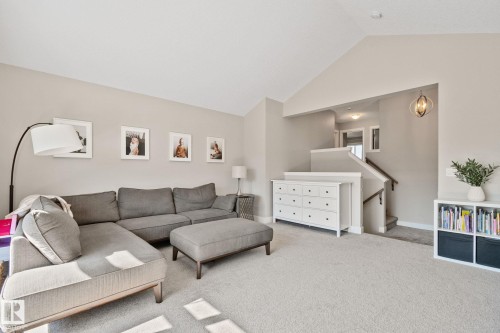Vaulted ceiling over carpeted living area, featuring a staircase with wood handrails and a decorative overhead light fixture - 2096 Redtail Common Nw, Edmonton, AB 