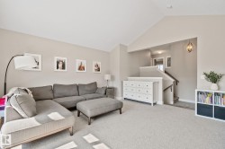 Vaulted ceiling over carpeted living area, featuring a staircase with wood handrails and a decorative overhead light fixture - 