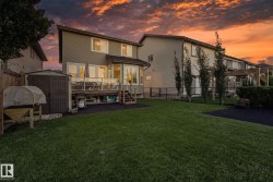 Expansive green lawn with a multi-level wood deck featuring glass railings, a built-in storage shed, and mature perimeter trees - 