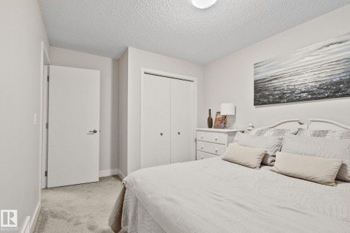 Neutral wall tones, textured ceiling, light-toned carpet flooring, white bi-fold closet doors, and a flush-mount ceiling light fixture - 2096 Redtail Common Nw, Edmonton, AB 