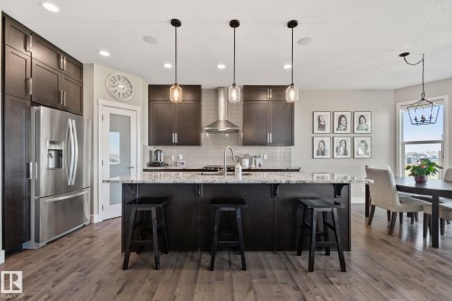 Kitchen featuring dark wood-finish cabinetry, stainless steel appliances, a large island with a light-toned countertop, pendant lighting, and wood-finish flooring - 2096 Redtail Common Nw, Edmonton, AB 