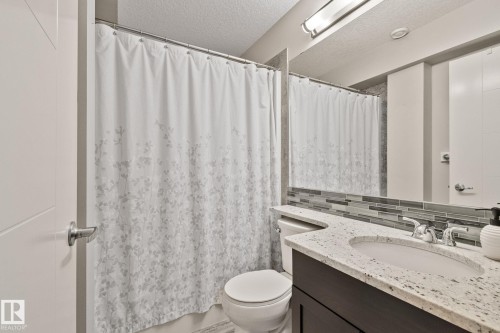 Bathroom featuring a vanity with an integrated sink, polished chrome faucet, and a stone-finish countertop - 2096 Redtail Common Nw, Edmonton, AB 