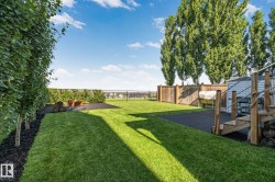 Expansive backyard featuring a lush lawn, mature trees, wood fencing, and a separate paved area - 
