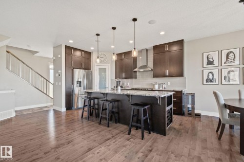 Kitchen with dark wood-finish cabinetry, stainless steel appliances, a multi-person island with a stone countertop, and wood-finish flooring - 2096 Redtail Common Nw, Edmonton, AB 