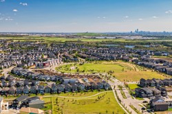 Expansive residential development featuring detached homes, green spaces, and a distant city skyline - 